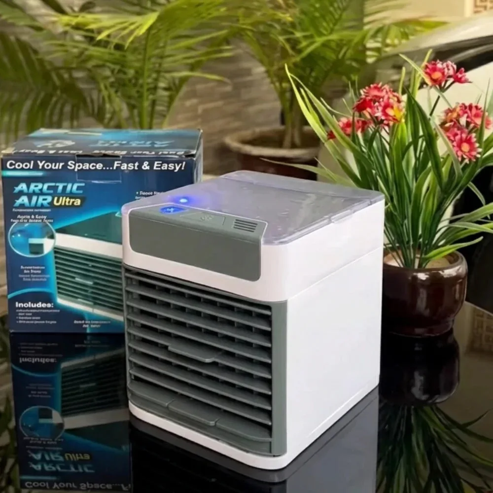 Arctic Air Ultra mini air cooler next to its retail packaging box on a table surrounded by plants